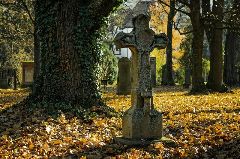 Steinkreuz im Herbstlaub Steinkreuz auf einem Friedhof zwischen herbstlichem Laub unter alten Bäumen