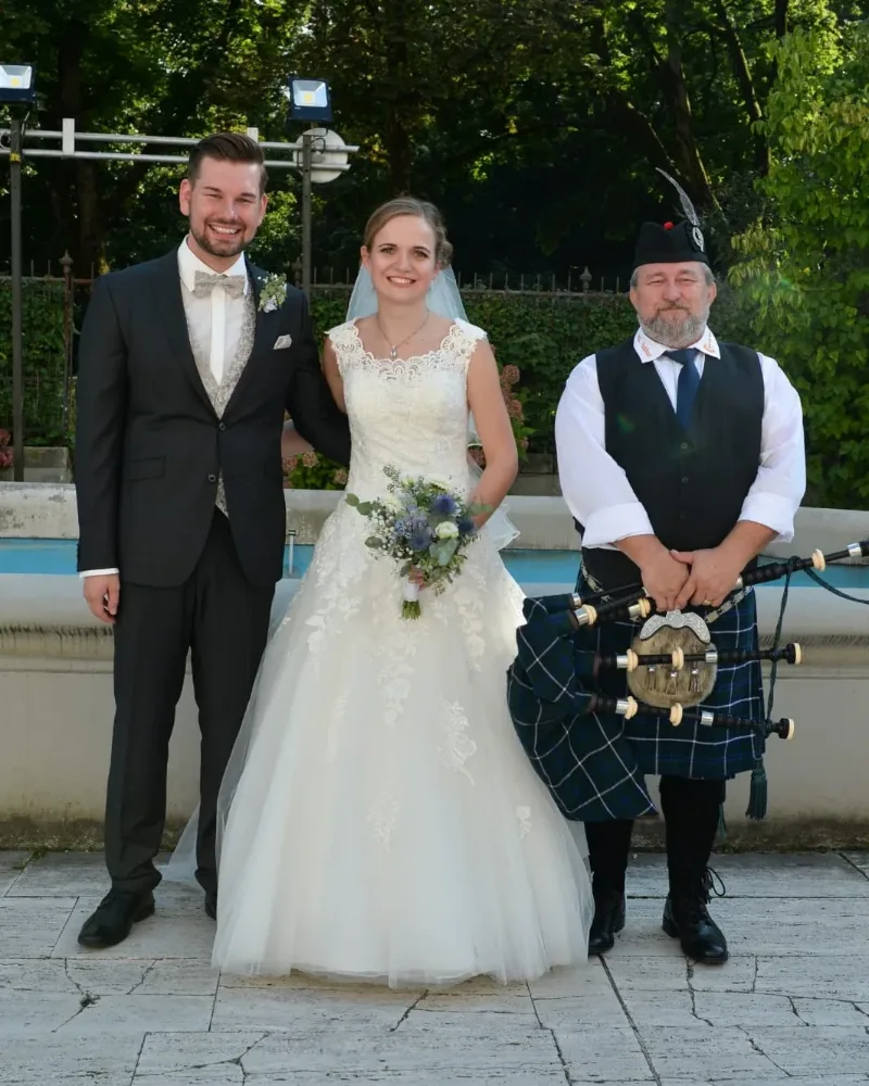Udo Zahlauer in Highland-Tracht mit Dudelsack neben einem lachenden Brautpaar