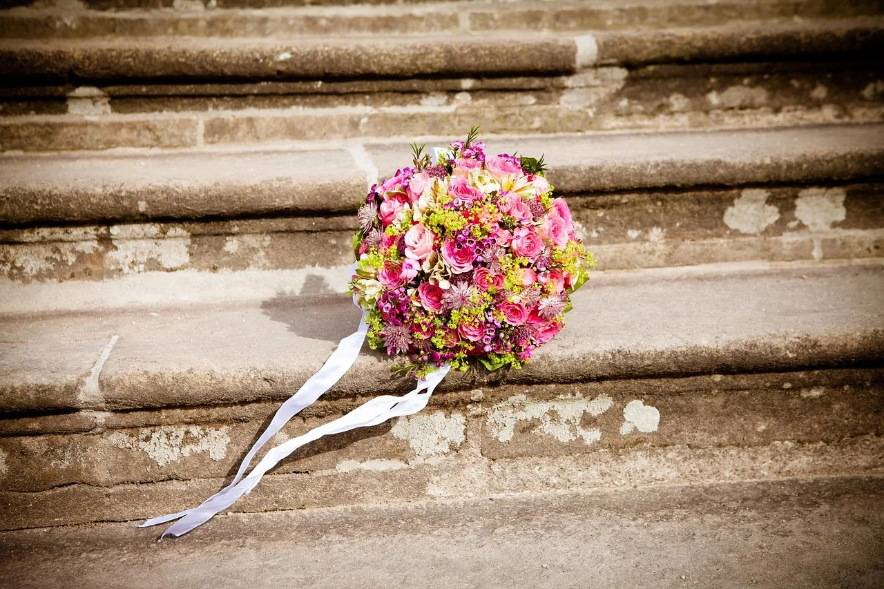 Hochzeitsstrauß aus rosa Rosen mit weißem Band auf steinernen Kirchenstufen